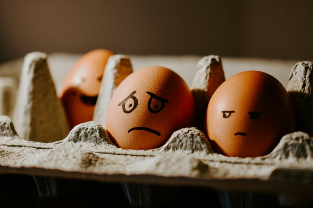 Eggs with drawn angry and frustrated faces in carton representing walking on eggshells in business relationships